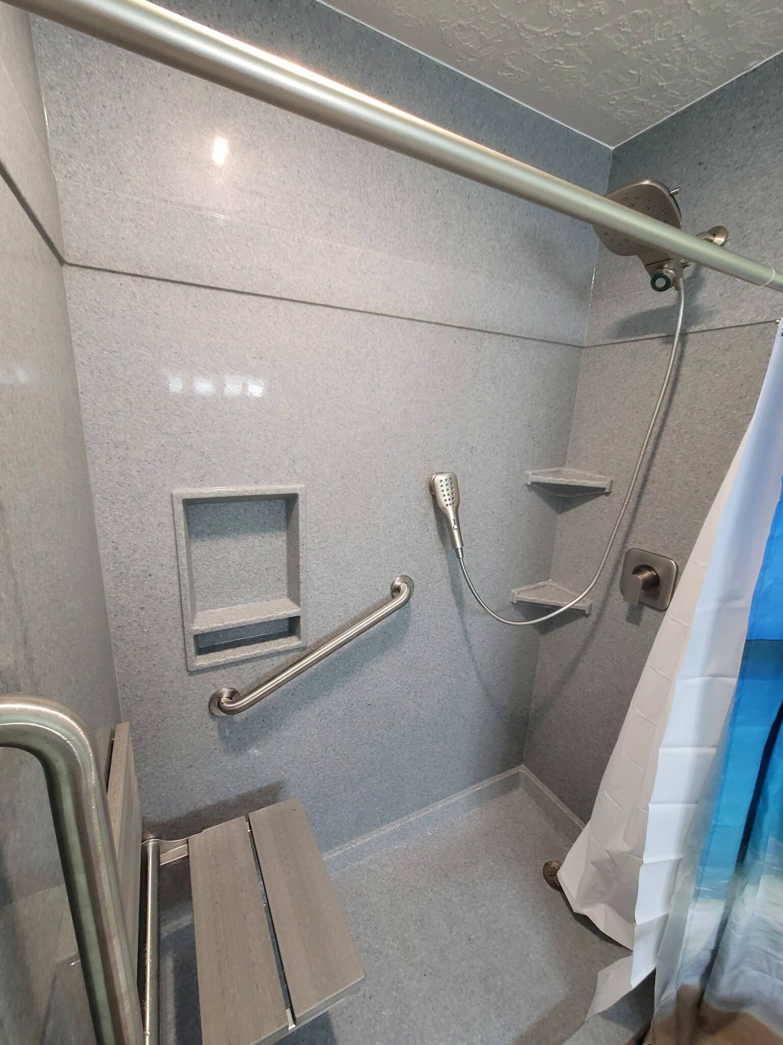 Accessible shower with speckled Onyx style walls, two grab bars, a fold down bench, a recessed niche and a handheld on a slide bar