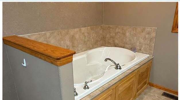 Before: a large corner jetted tub with an oak surround taking up most of the room