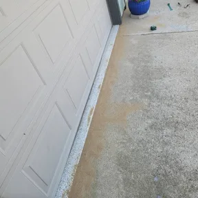 A concrete apron and driveway run beside a garage, with a fresh sealant line along the joint