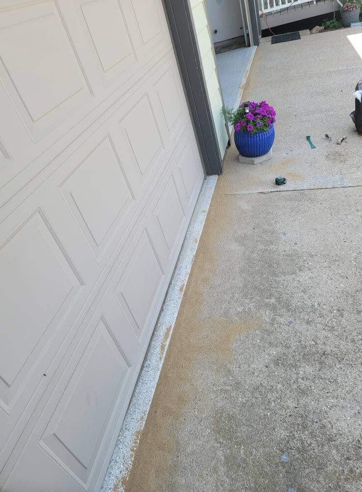 A concrete apron and driveway run beside a garage, with a fresh sealant line along the joint