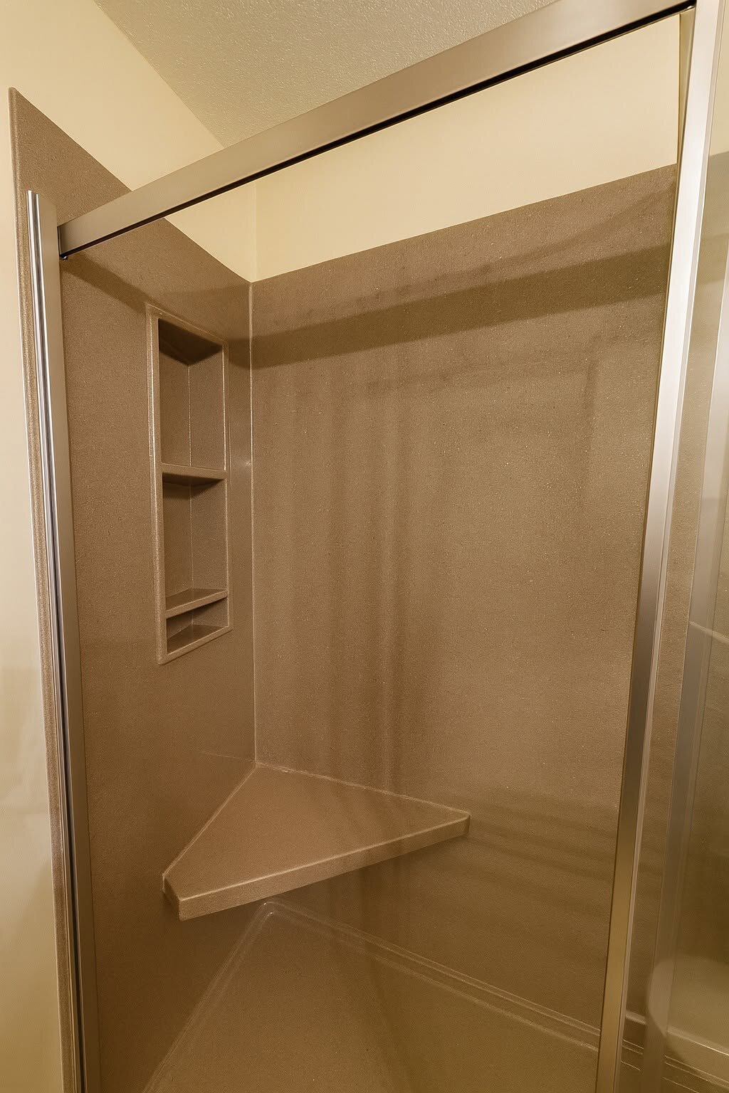 Tan solid-surface shower with a corner shelf and sliding door.