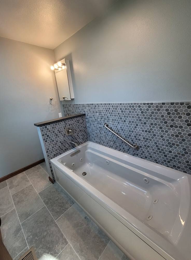 Jetted tub with a hex-mosaic wall and a real grab bar, not an afterthought.