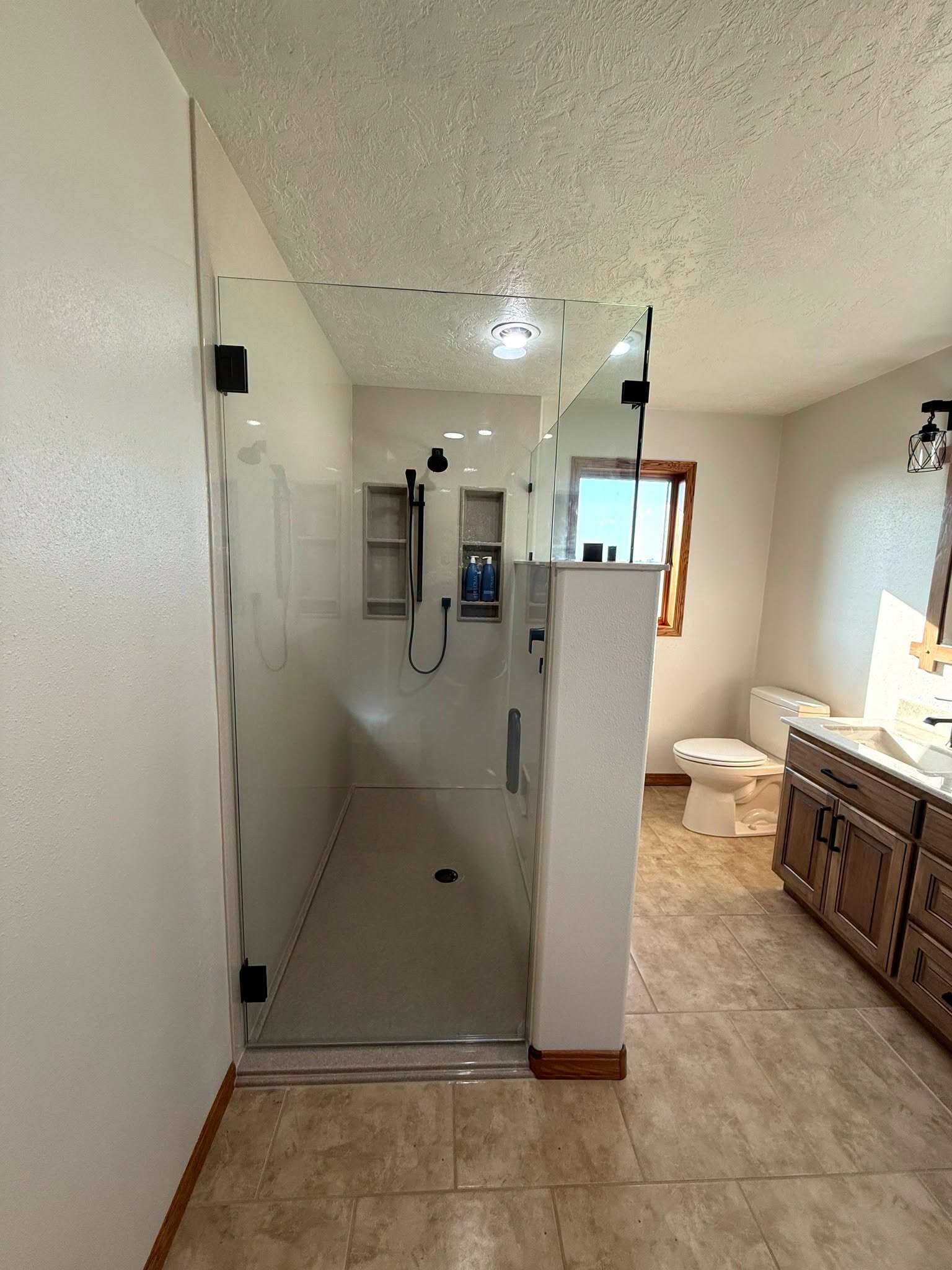 Frameless walk-in, black hardware, two niches cut into the wall.