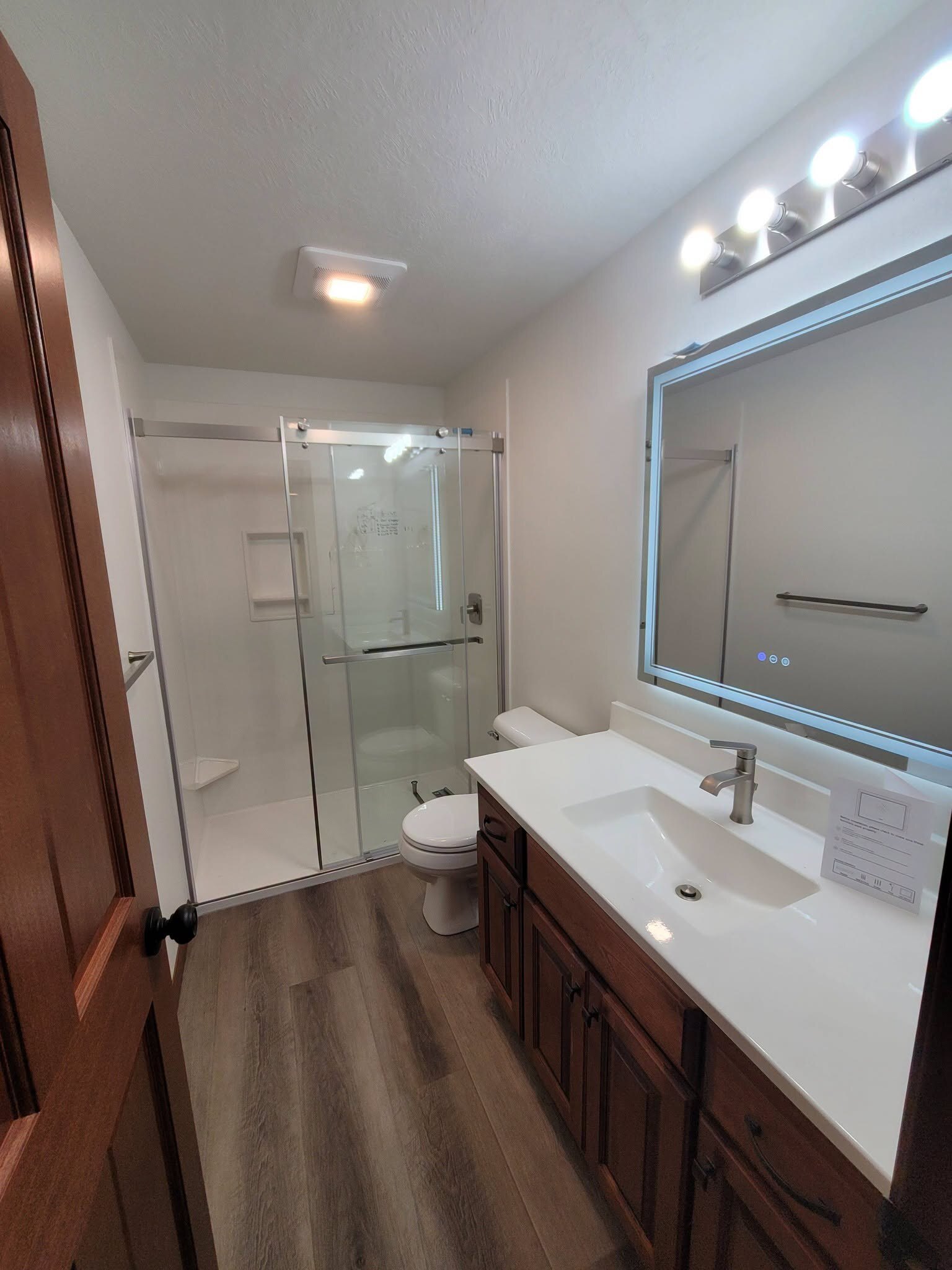 Sliding glass shower, backlit mirror, wood vanity.