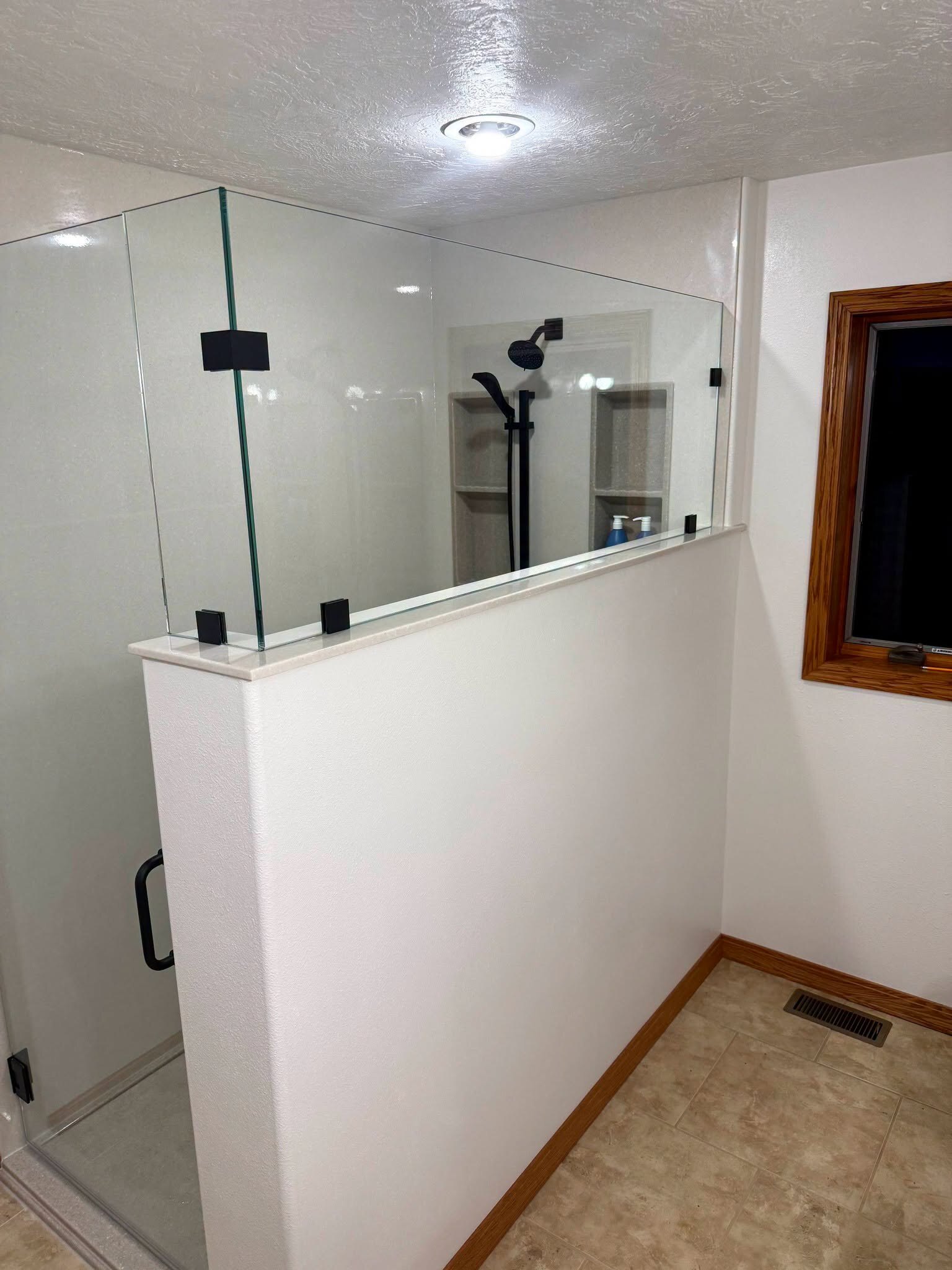 We built this glass half-wall shower with black hardware and tile niches.