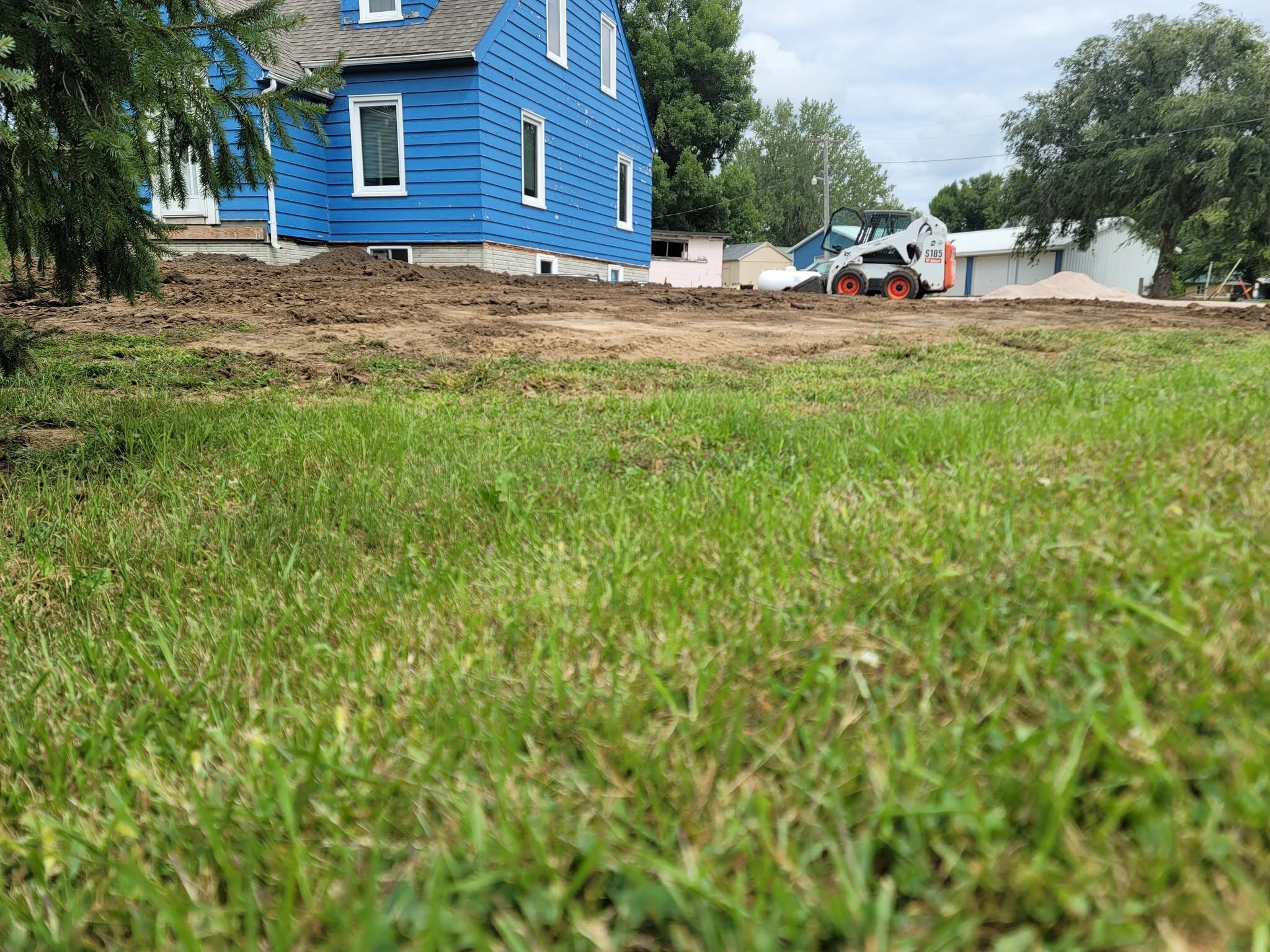 The skid steer is on the grade with the house behind it.
